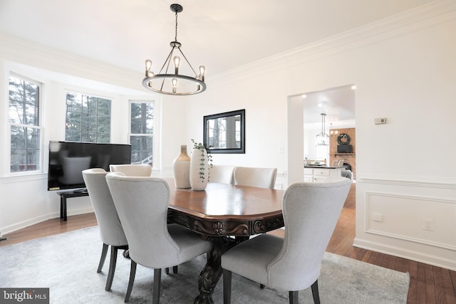 dining space with a chandelier, ornamental molding, a fireplace, and wood finished floors