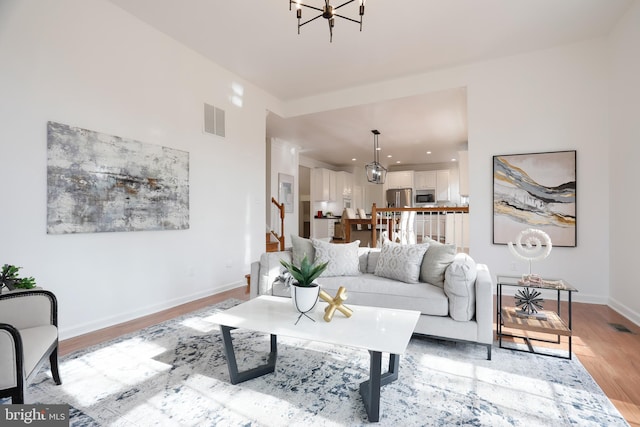 living room featuring visible vents, light wood-style flooring, stairway, an inviting chandelier, and baseboards