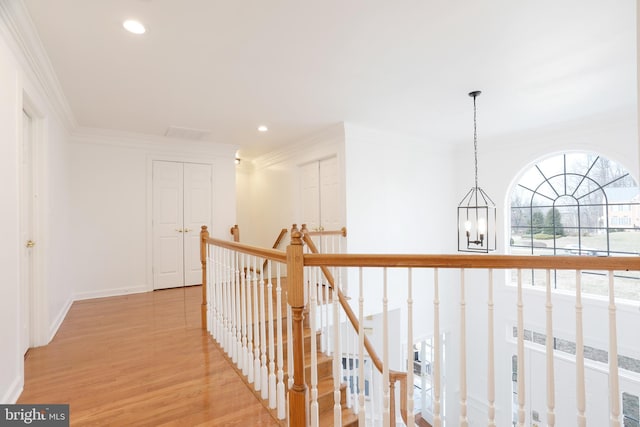 hall featuring light wood finished floors, recessed lighting, ornamental molding, a notable chandelier, and an upstairs landing