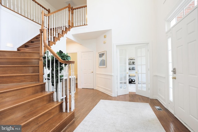 foyer entrance featuring stairs, a decorative wall, wood finished floors, and a towering ceiling