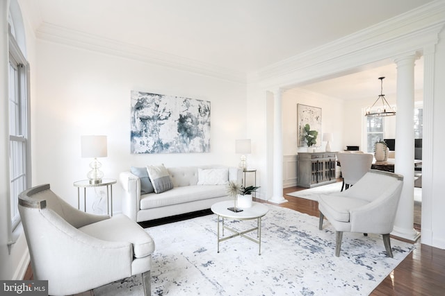 living room featuring crown molding, wood finished floors, ornate columns, and a chandelier