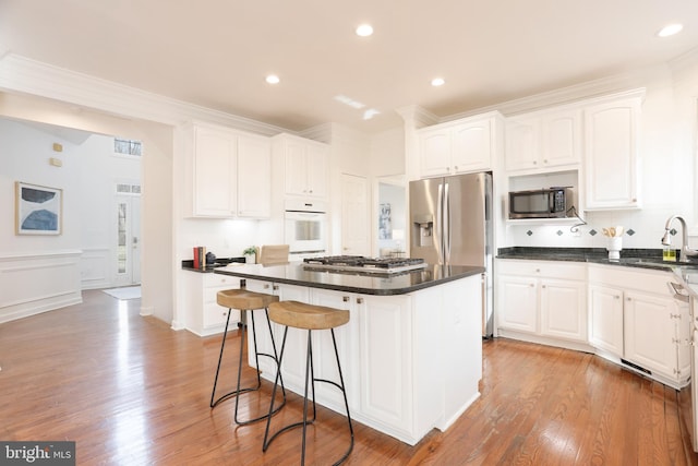 kitchen featuring dark countertops, a center island, crown molding, appliances with stainless steel finishes, and white cabinets