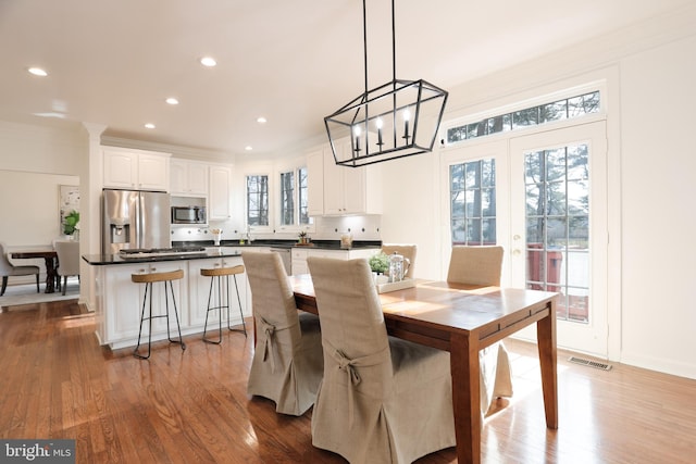 dining room with wood finished floors, visible vents, french doors, and ornamental molding