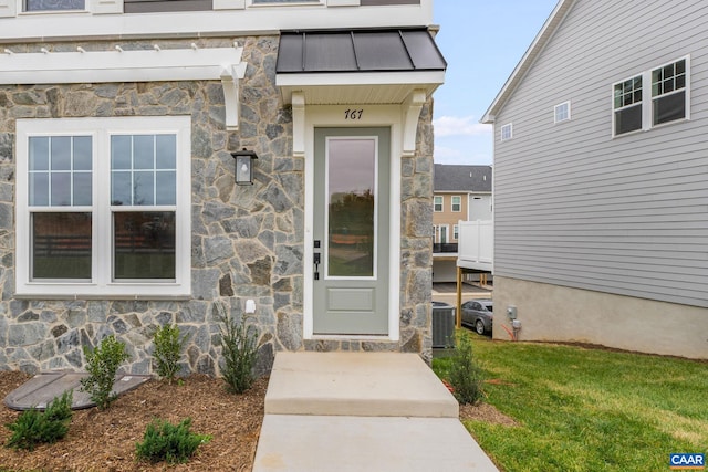 doorway to property with central AC unit, metal roof, a yard, stone siding, and a standing seam roof