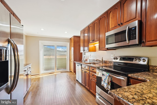 kitchen with light wood-style flooring, dark stone countertops, a sink, stainless steel appliances, and crown molding