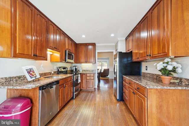 kitchen with light stone countertops, light wood finished floors, ornamental molding, appliances with stainless steel finishes, and brown cabinets