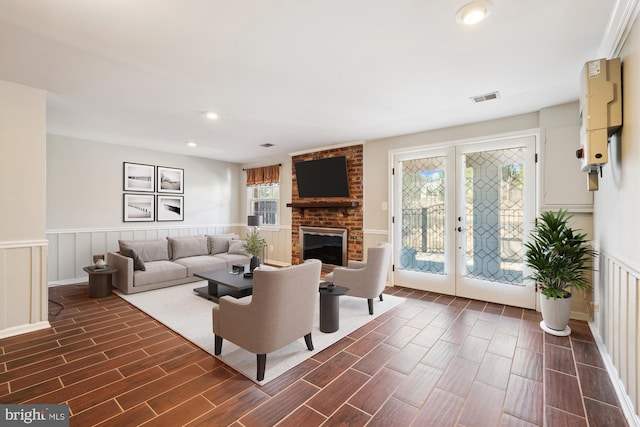 living room featuring visible vents, a brick fireplace, wood finish floors, and a wainscoted wall