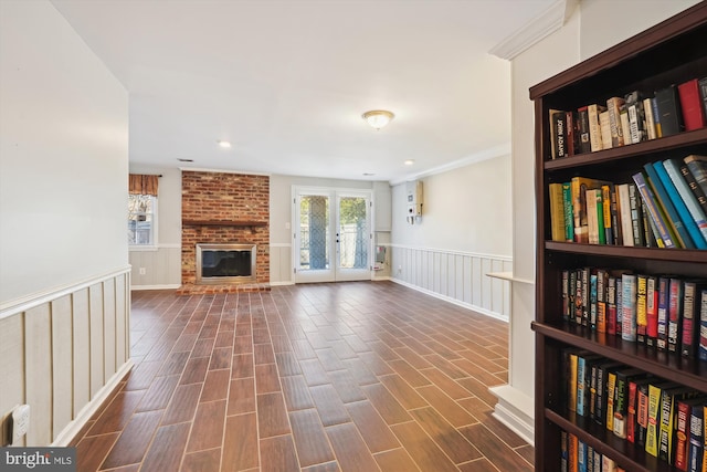 unfurnished living room with wood finish floors, a fireplace, french doors, wainscoting, and crown molding