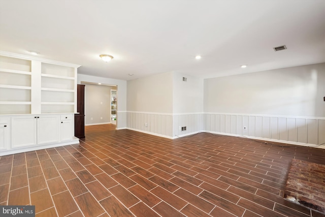 unfurnished room with a wainscoted wall, dark wood-type flooring, and visible vents