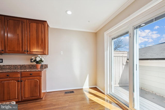 interior space featuring light wood finished floors, visible vents, crown molding, baseboards, and dark stone counters