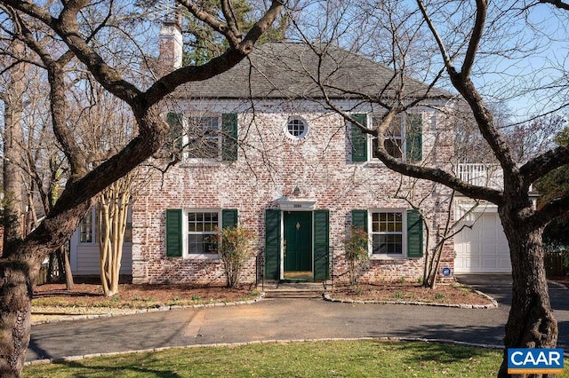 colonial house with aphalt driveway, brick siding, a garage, and a chimney