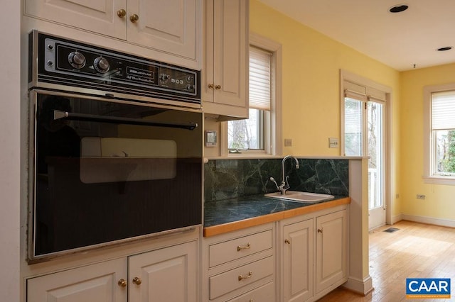 kitchen featuring decorative backsplash, black oven, white cabinetry, and a sink