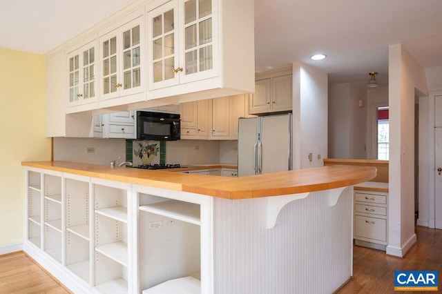 kitchen featuring wooden counters, a peninsula, light wood-style flooring, black appliances, and glass insert cabinets