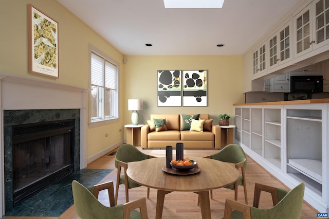 living room featuring baseboards, light wood-style floors, a skylight, and a high end fireplace