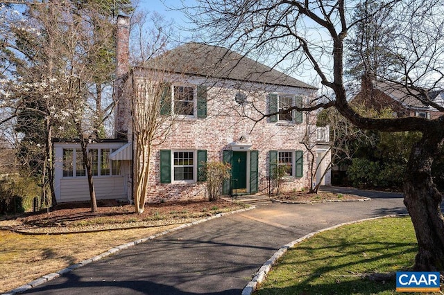 view of front facade featuring brick siding, driveway, and a chimney