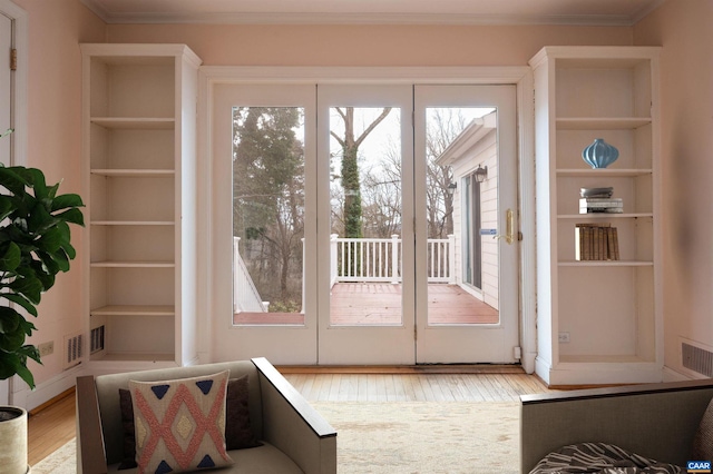 doorway with built in features, visible vents, wood finished floors, and ornamental molding