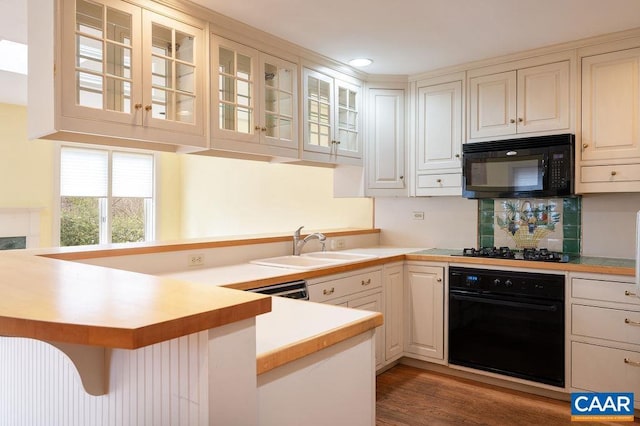 kitchen featuring a peninsula, a sink, black appliances, light countertops, and glass insert cabinets