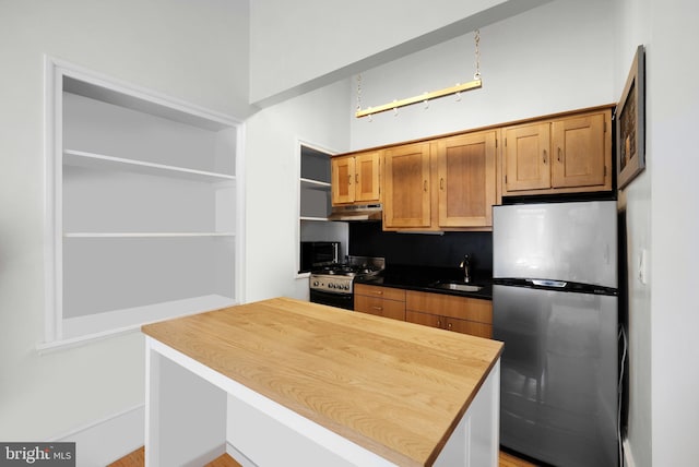 kitchen featuring under cabinet range hood, open shelves, appliances with stainless steel finishes, and a sink