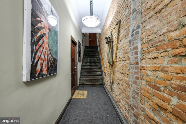 hall featuring baseboards, carpet, brick wall, and stairs