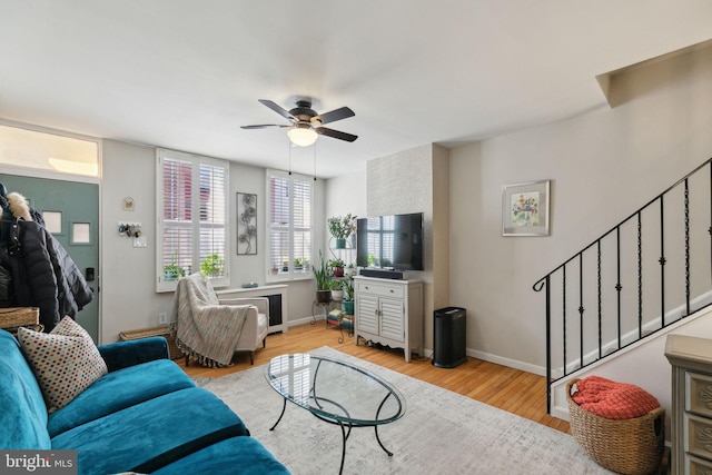 living area with stairway, a ceiling fan, baseboards, and wood finished floors