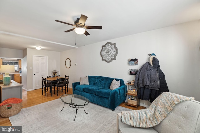 living area featuring ceiling fan, baseboards, and light wood-style flooring