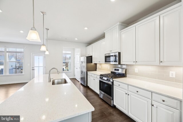 kitchen with a sink, dark wood-style floors, appliances with stainless steel finishes, white cabinets, and decorative backsplash