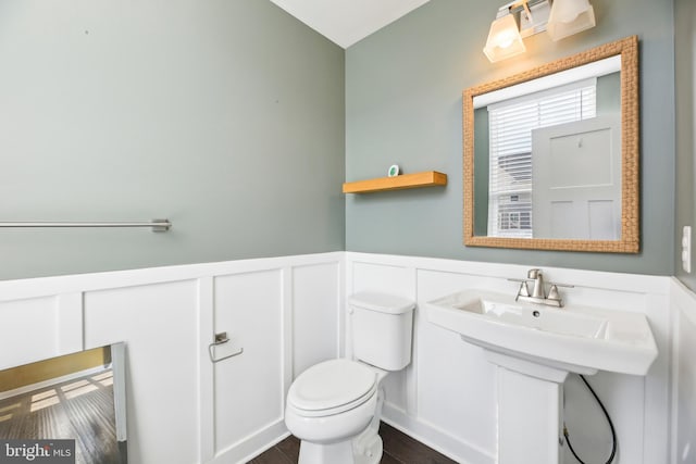 half bathroom with a decorative wall, wainscoting, and toilet