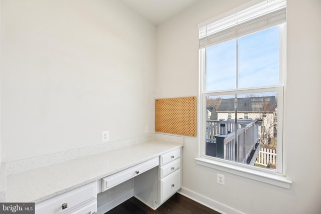 unfurnished office featuring built in desk, dark wood-type flooring, and baseboards