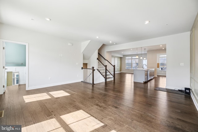 unfurnished living room featuring baseboards, stairs, dark wood-style flooring, recessed lighting, and a sink