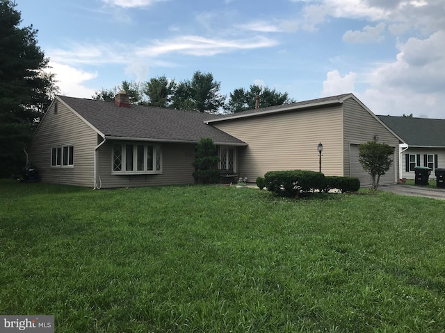 view of front of house featuring an attached garage, a chimney, a front lawn, and a shingled roof