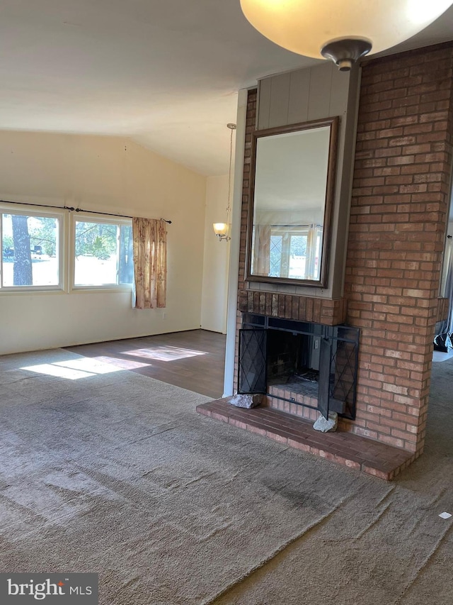 unfurnished living room with carpet flooring, a brick fireplace, and vaulted ceiling