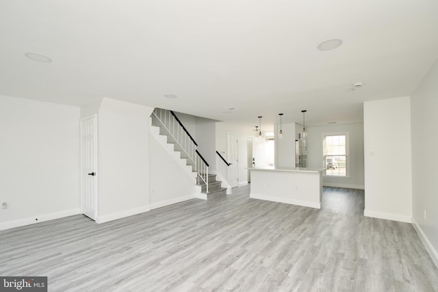 unfurnished living room with stairs, baseboards, and light wood-type flooring