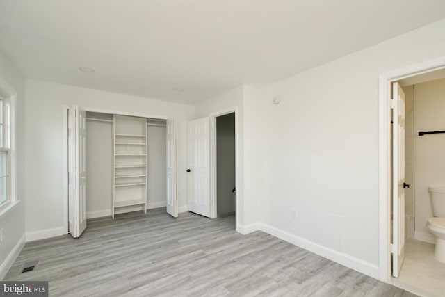 unfurnished bedroom featuring visible vents, connected bathroom, baseboards, wood finished floors, and a closet