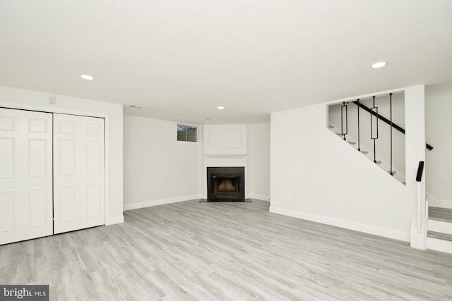 finished basement with a fireplace with flush hearth, recessed lighting, stairway, light wood-style floors, and baseboards