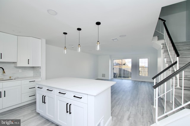 kitchen with backsplash, light wood-style floors, hanging light fixtures, white cabinetry, and a sink