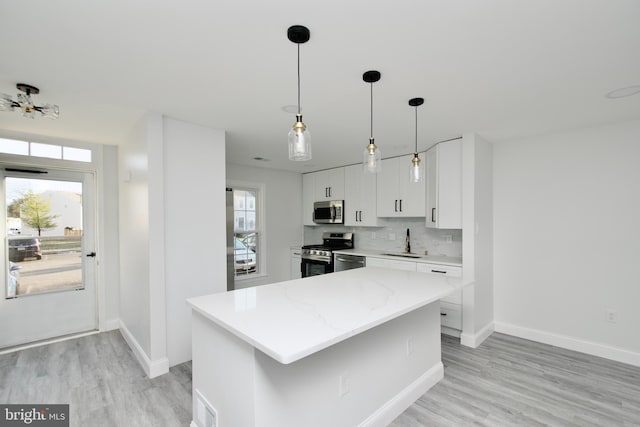 kitchen with a sink, decorative backsplash, stainless steel appliances, white cabinets, and light wood-type flooring