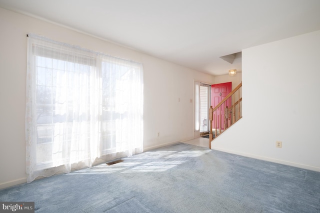 carpeted spare room with stairs, baseboards, and visible vents