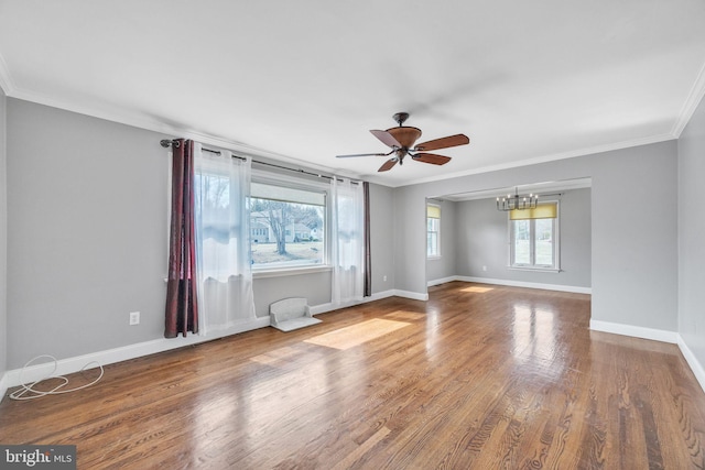 empty room with ceiling fan with notable chandelier, wood finished floors, baseboards, and ornamental molding