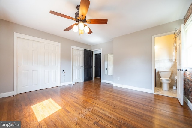 unfurnished bedroom featuring ensuite bath, wood finished floors, baseboards, and two closets