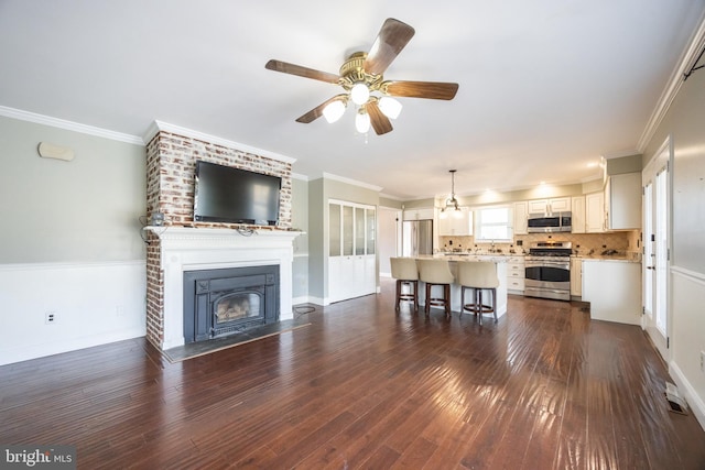 unfurnished living room featuring dark wood finished floors, crown molding, a ceiling fan, and a large fireplace