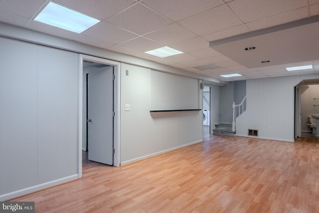 basement with visible vents, a drop ceiling, stairs, light wood-style floors, and arched walkways