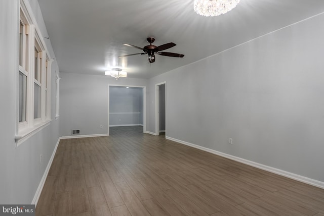 unfurnished room featuring visible vents, baseboards, wood finished floors, and ceiling fan with notable chandelier