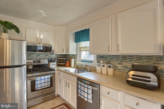 kitchen with white cabinets, stainless steel appliances, light countertops, and a sink