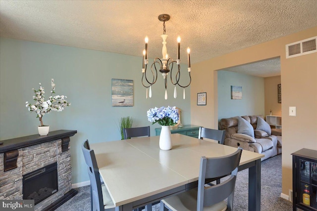 carpeted dining area featuring visible vents, baseboards, a stone fireplace, a notable chandelier, and a textured ceiling