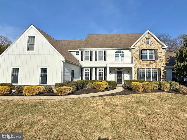 view of front facade featuring stone siding, roof with shingles, board and batten siding, and a front lawn