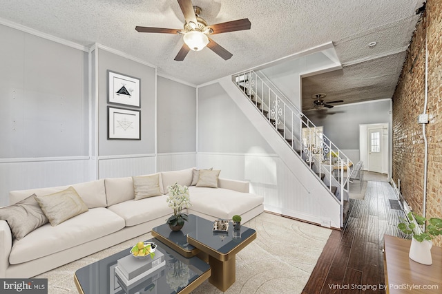 living area with stairway, wood finished floors, brick wall, a textured ceiling, and crown molding