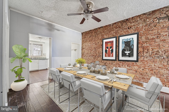 dining room with a wainscoted wall, a textured ceiling, wood finished floors, brick wall, and crown molding