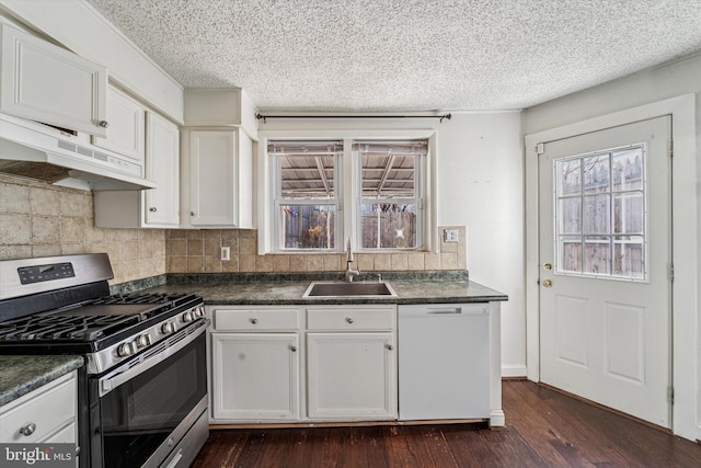 kitchen with stainless steel gas stove, a sink, under cabinet range hood, dark countertops, and white dishwasher