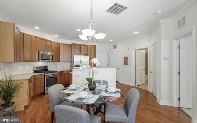 dining space featuring visible vents, a notable chandelier, wood finished floors, and ornamental molding