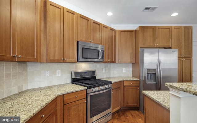 kitchen featuring visible vents, backsplash, wood finished floors, stainless steel appliances, and brown cabinetry